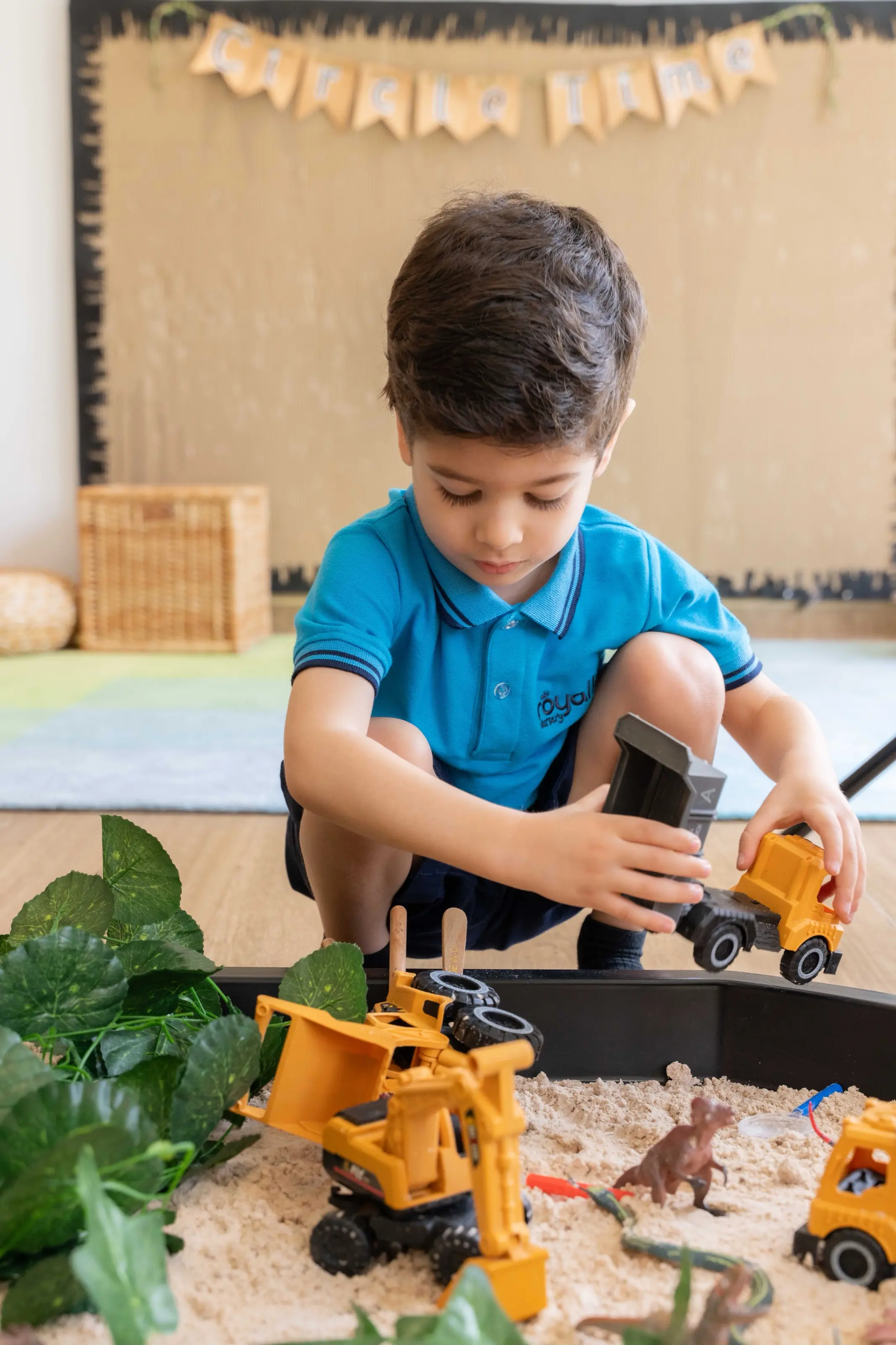 A preschool child playing with diggers at a sand tray